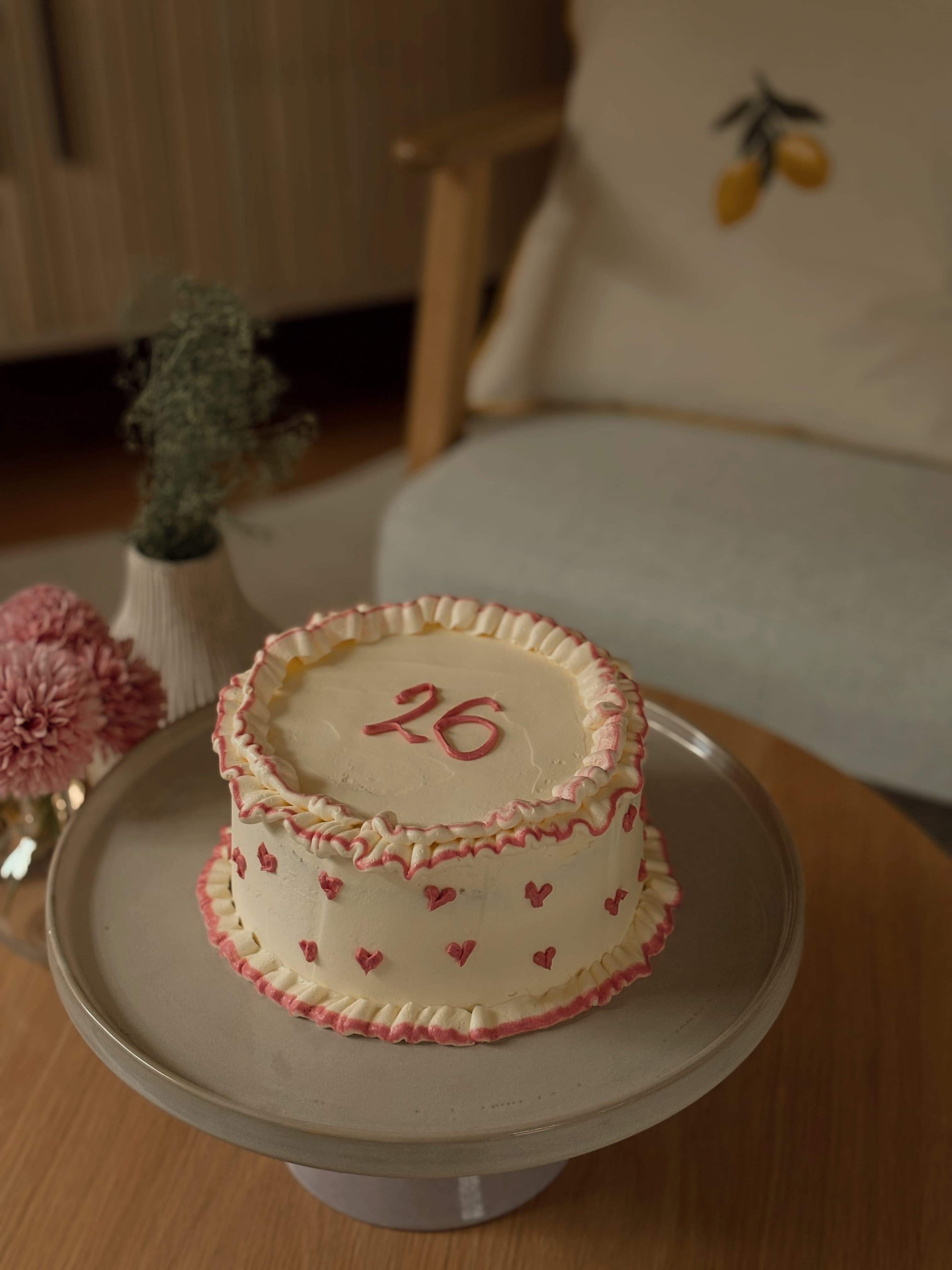Vintage-stil 26-årskake med rosa hjerter og piping, stilt opp i hjemmemiljø med blomster